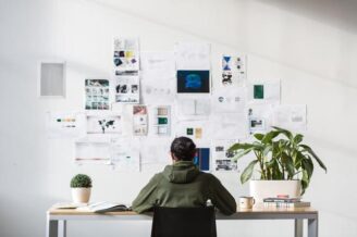 man sitting at desk working on computer with plants and papers on wall