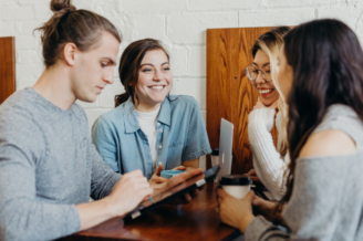 Four women sitting around table laughing with phones