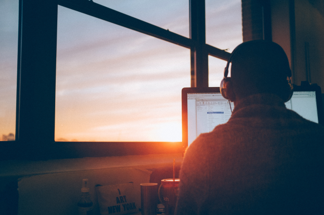 man sitting at desk working on computer next to window