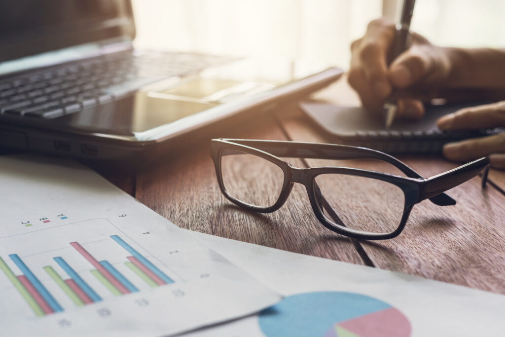 Business person's hand writing on notebook with printed graphs and charts on the desk