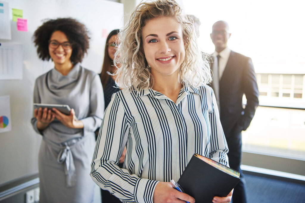 smiling businesswoman standing at the forefront with other business people in background after meeting about generating leads