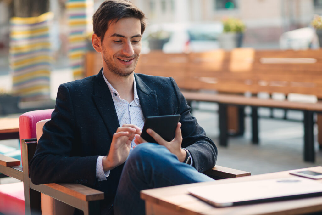 Successful business worker is reading news on web via digital tablet, sitting on chair with leg over leg.