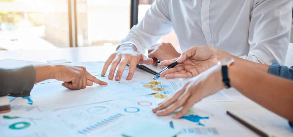 Hands of 3 business professionals reviewing papers about a multi-channel selling strategy