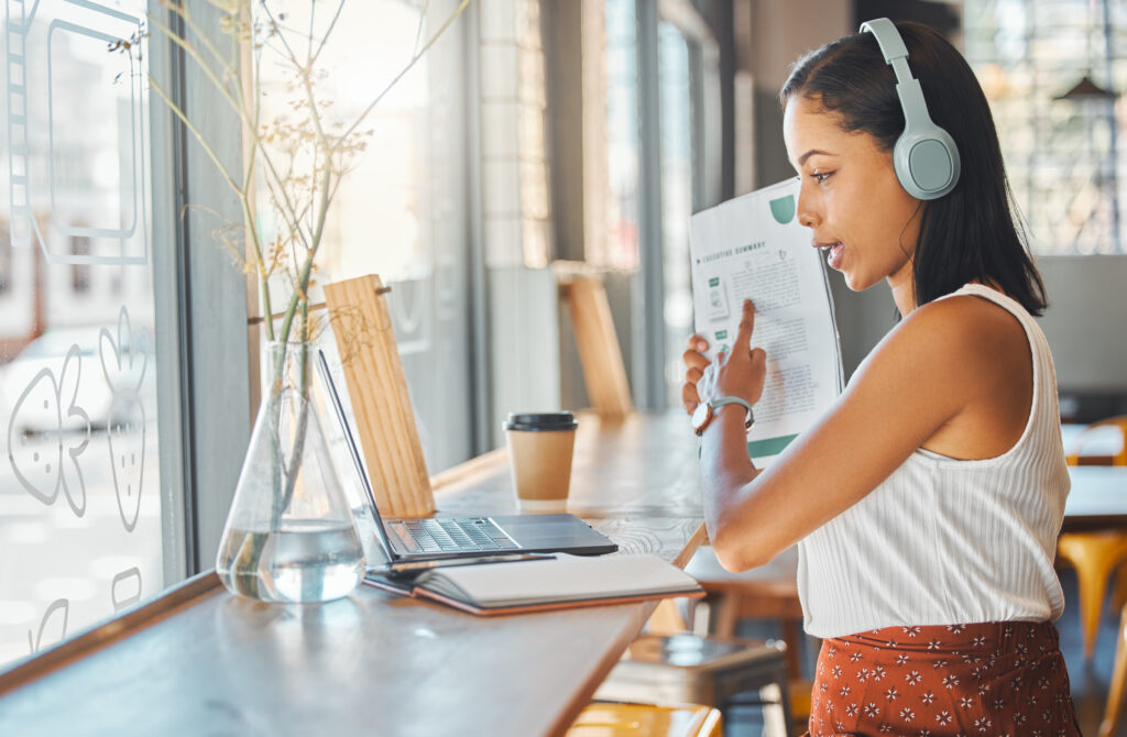 Businesswoman stands in front of laptop holding up a visual aid as she presents a demo to a Zoom audience