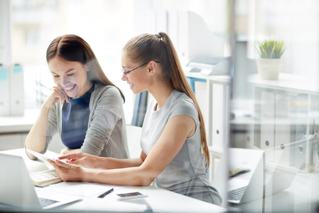 Two businesswomen sit together at a desk reviewing the results of their relationship intelligence analysis