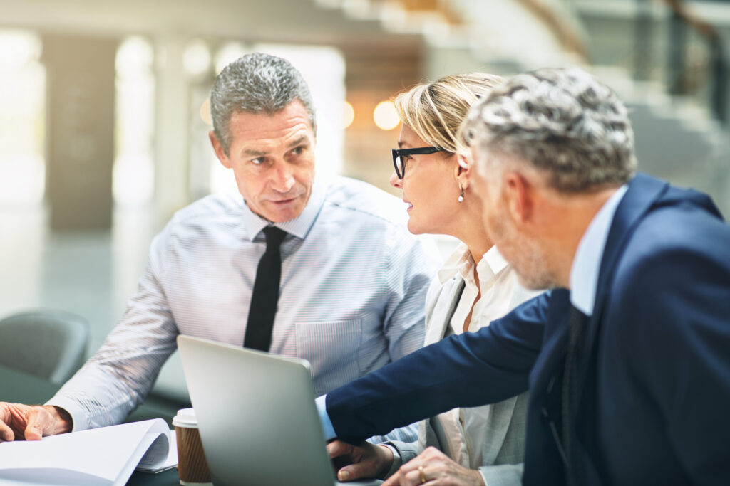 Two businessmen and one business woman sit at a conference desk talking with a laptop in front of them going over the new framework for EU-US data flows