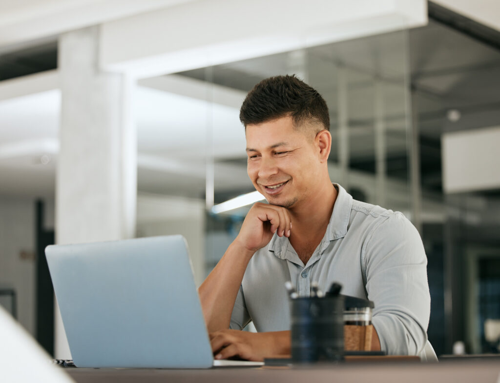 salesman sitting at desk in front of laptop computer smiling as he works on AI cold outreach
