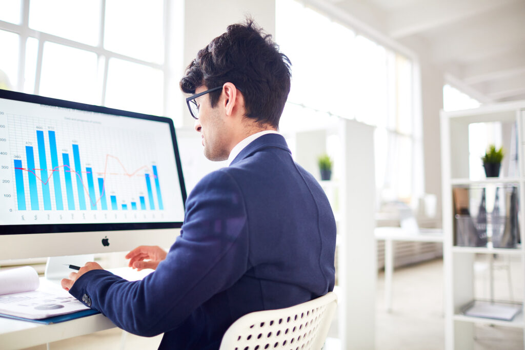 businessman sits at a desk typing on the computer and looking at sales analytics data