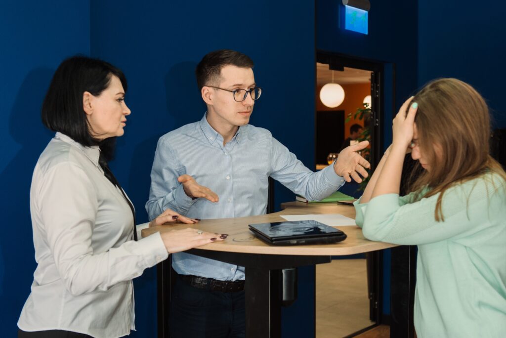Group of three colleagues stand talking at a table trying to comfort one coworker who is upset about an outbound sales mistake