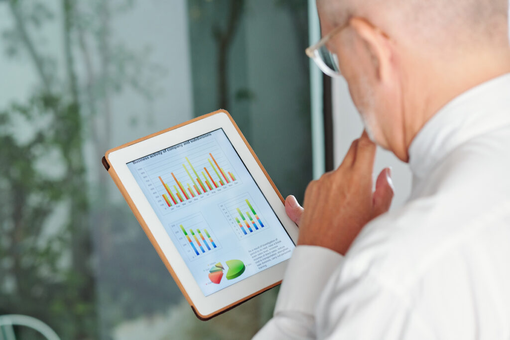 a close-up shot of the back of a man's head looking at a tablet showing data from sales