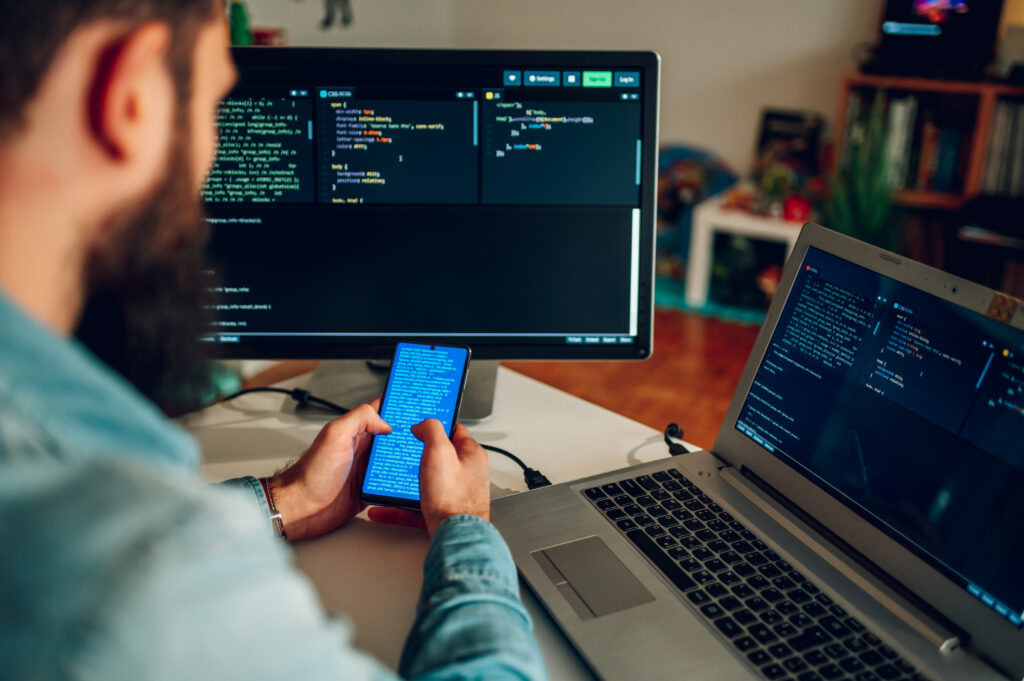 cybersecurity professional sits in front of two screens looking at phishing email on his smartphone