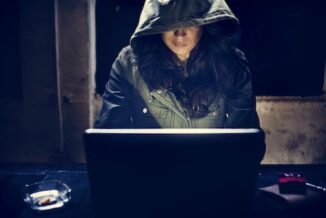 Hacker sitting at a laptop working on email phishing scam