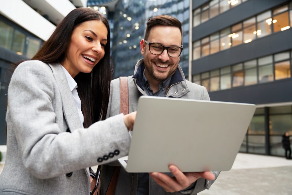 Two business professionals stand outside office building looking at a laptop showing B2B lead generation tools