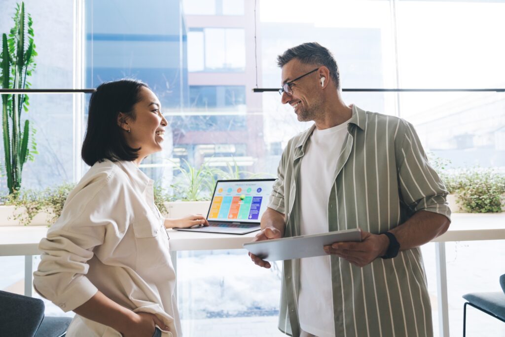 Two business professionals stand in front of a desk talking animatedly about B2B visitor intelligence