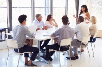A businesswoman stands in front of colleagues at a conference table discussing B2B lead generation campaigns
