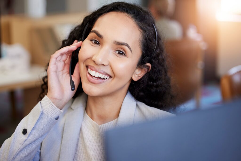 Photograph of a woman's face and torso wearing a headset smiling as she makes sales calls