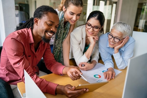 Group of business professionals stand over a desk together looking at a computer screen as they discuss lead magnet creation