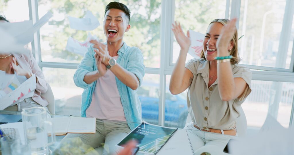 Group of co-workers sit around table laughing and clapping, celebrating a team win in account-based marketing for B2B