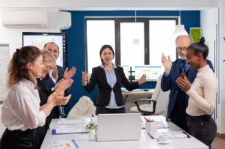 Marketing team stands around a conference table clapping in celebration of their ABM program success.