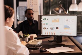 Two professionals sit at a desk, with a desktop screen showing metrics from an AI for B2B sales tool