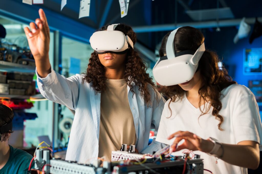 Two women wear VR glasses while working on robotics