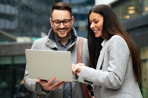 Two business professionals stand together looking at a laptop smiling talking about multi-channel sales.