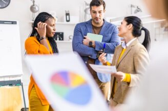 Group of business professionals stand looking at sales charts discussing behavioral data and sales