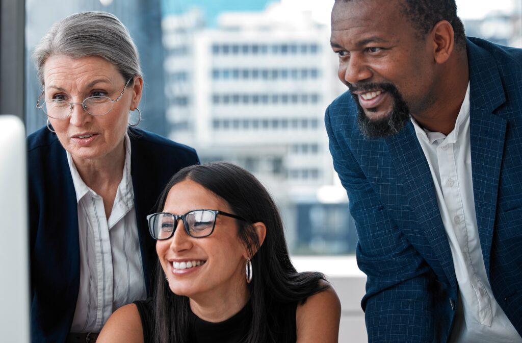 Group of 3 business people stand looking at a computer screen smiling as they discuss LinkedIn data analytics