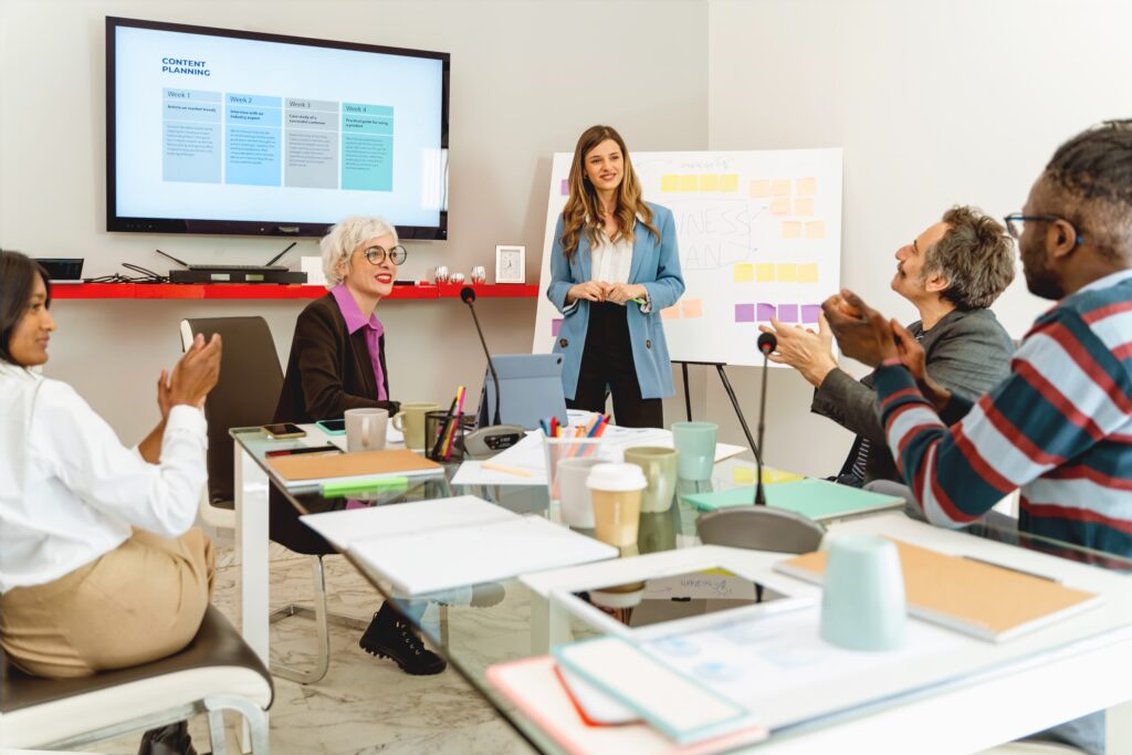 Group of business people sit around a conference table watching a businesswoman presenting about social media engagement metrics