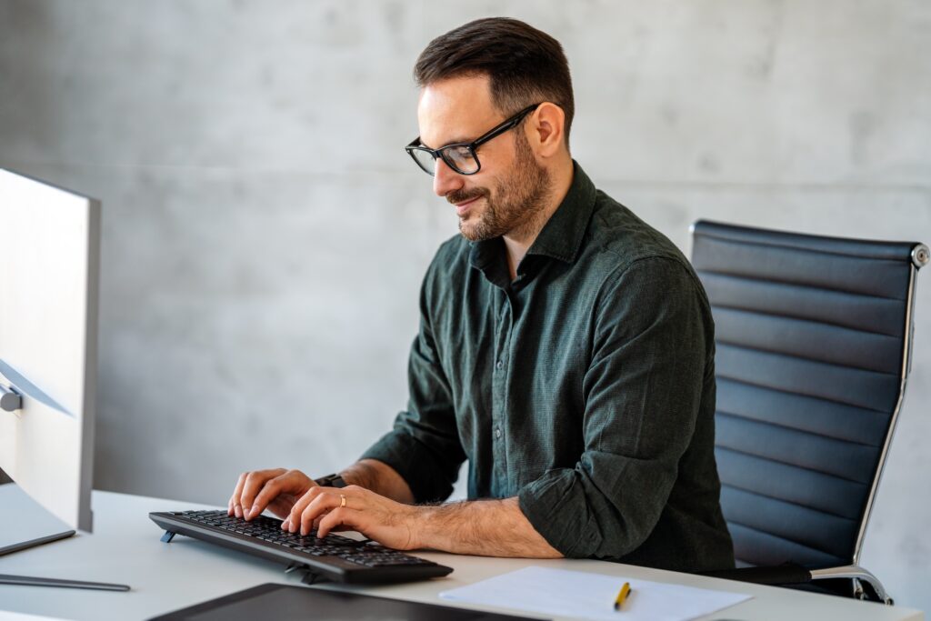 Business man sits at desk in front of a desktop computer, typing tailored outreach as part of a B2B personalization strategy