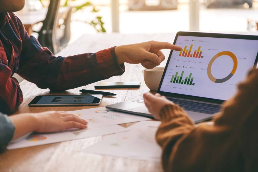 The hands of two business people point at charts on a laptop discussing B2B lead generation campaigns metrics